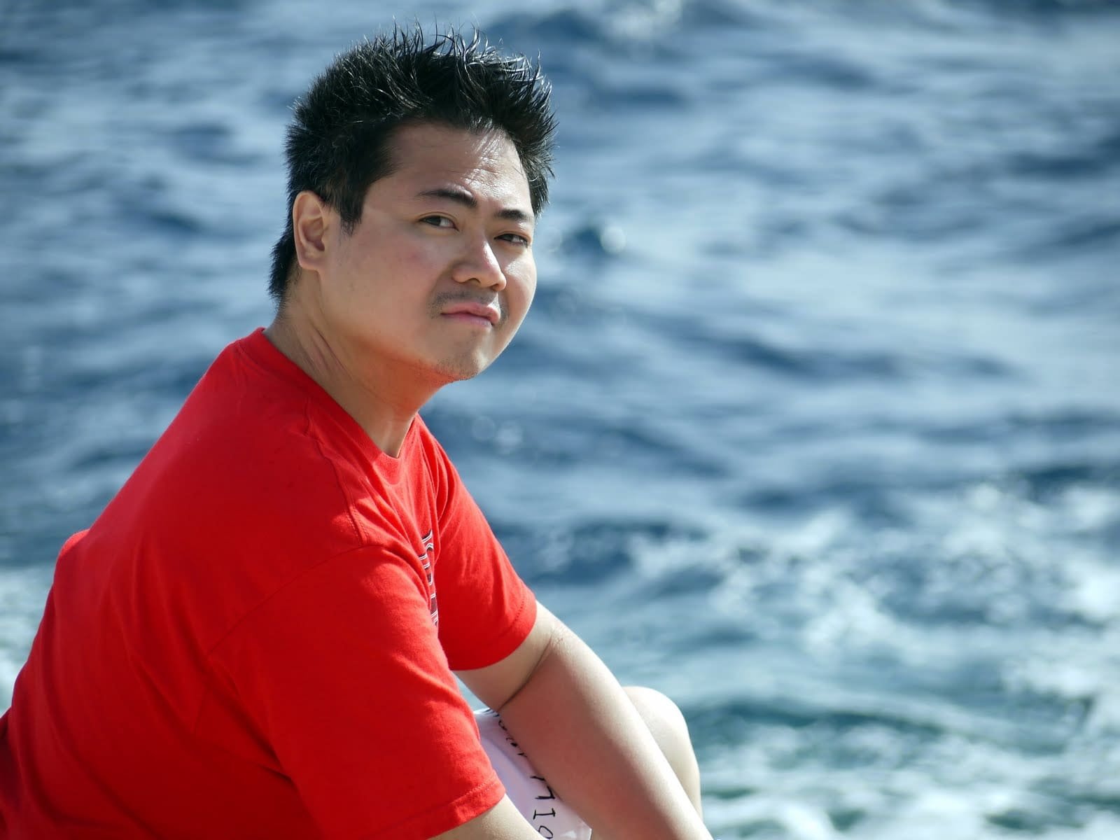 Me by the sea in a red t-shirt, at the heavier end of a swing.